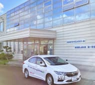 校舎の前を走る教習車。校舎は一部ガラス張り＆白が基調です。